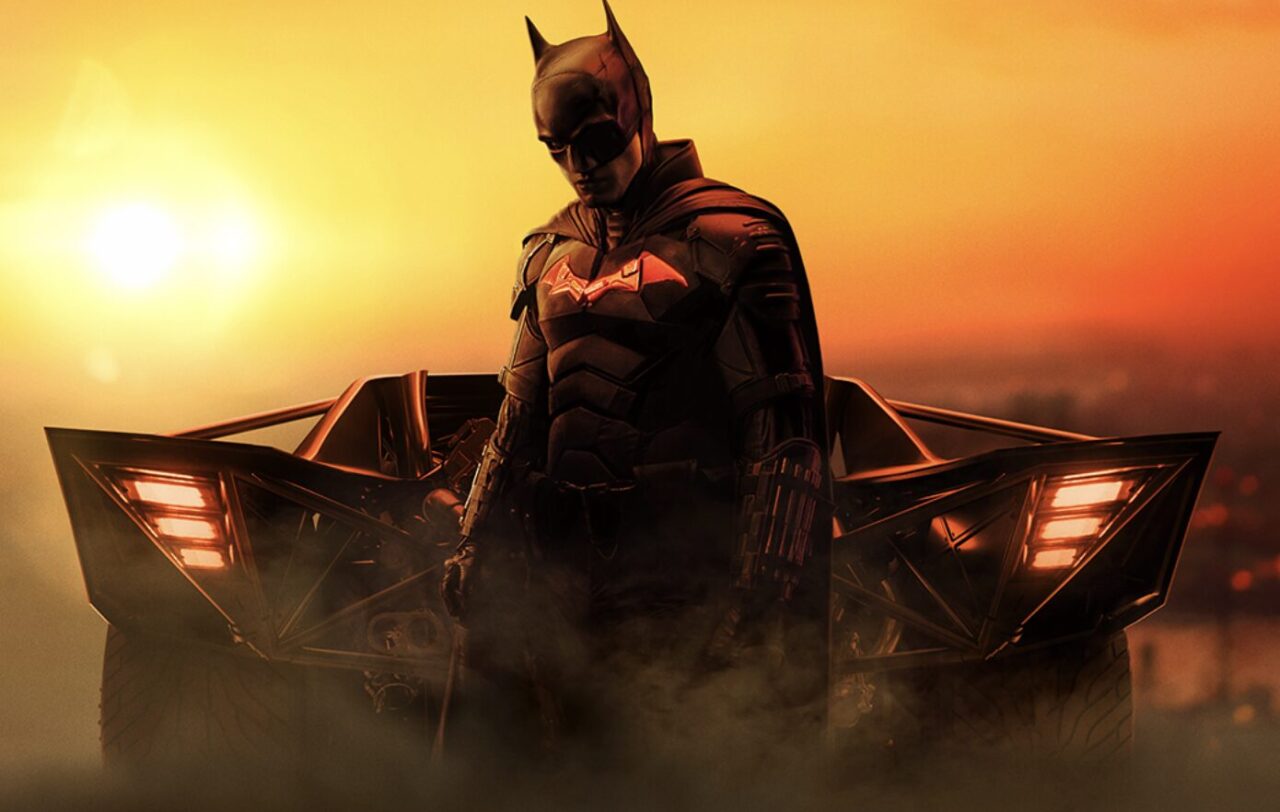 『THE BATMAN－ザ・バットマン－』のバットマンが夕焼けの中で車の前に立つ公式キービジュアル（Elseworldsの象徴）
